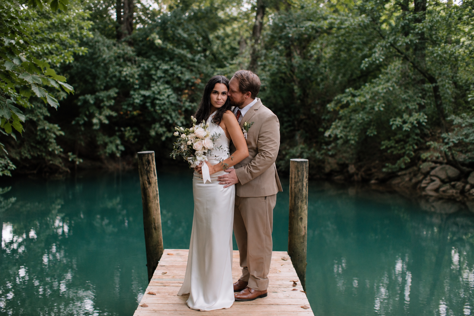 Newlyweds standing together on the dock beside the blue spring