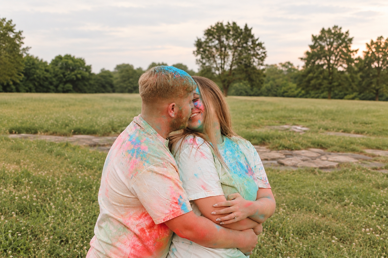 An expectant couple sharing a joyful moment covered in colorful powder on the estate grounds